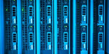 Responsável de TI conferindo o painel de rotina de backup enquanto a equipe da empresa segue operando ao fundo